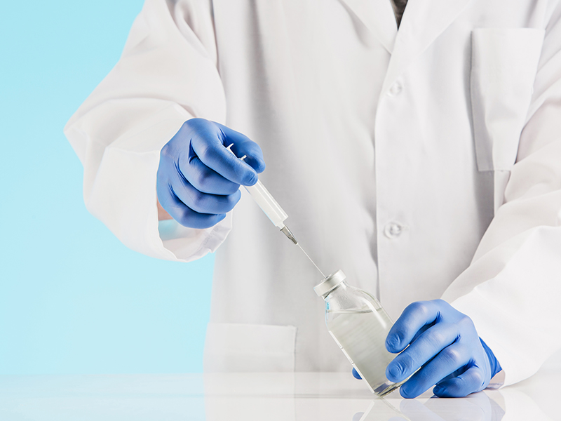Hand in a blue glove holding syringe on blue background