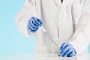 Hand in a blue glove holding syringe on blue background