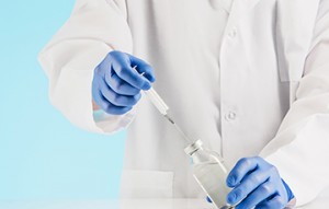 Hand in a blue glove holding syringe on blue background